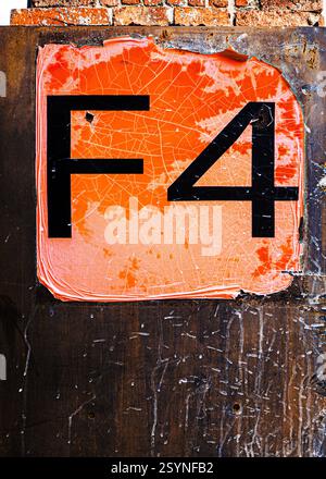 Close-up of a worn-out orange industrial sign with black “F4” lettering, cracked paint, and rusted edges on a metal surface, showing decay and texture Stock Photo
