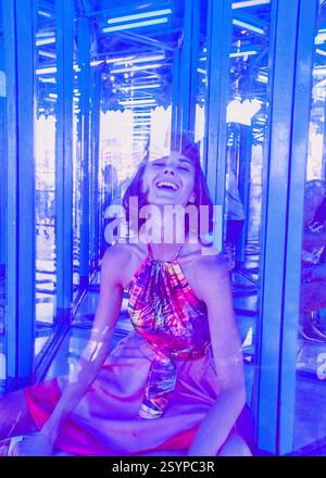 Sweet caucasian young woman sitting and posing in a mirror maze with and enjoys an unusual attraction room in amusement park. Stock Photo