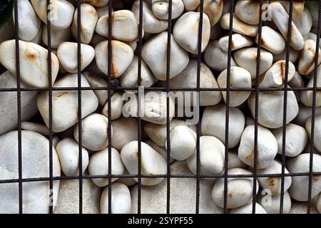 A stone wall consisting with white pebbles behind the iron mesh which can be used as a background for the monitor of the computer. Stock Photo
