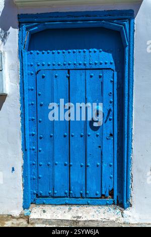 weathered wooden door painted a vibrant blue, adorned with metal studs and a ring pull handle, creating a visually rich and texturally interesting ent Stock Photo