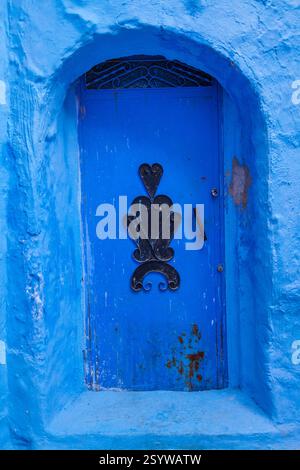 weathered wooden door painted a vibrant blue, adorned with metal studs and a ring pull handle, creating a visually rich and texturally interesting ent Stock Photo