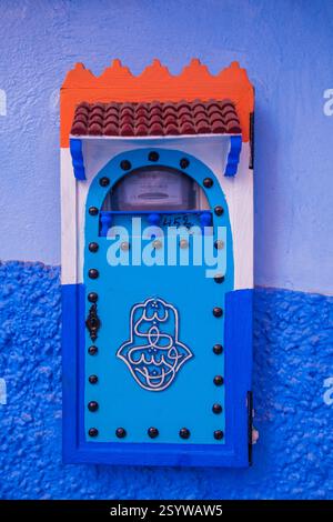 brightly colored, decorative utility box, possibly a meter or electric box, with a hamsa hand symbol, mounted on a textured blue wall Stock Photo