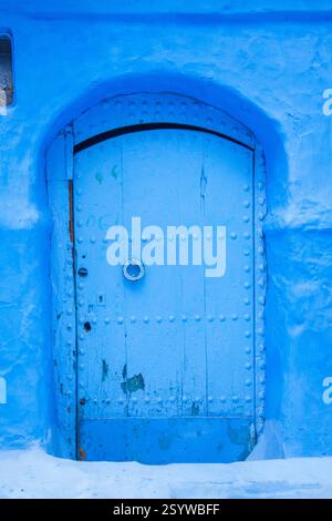 blue arched wooden door with decorative studs, set within a textured blue wall Stock Photo