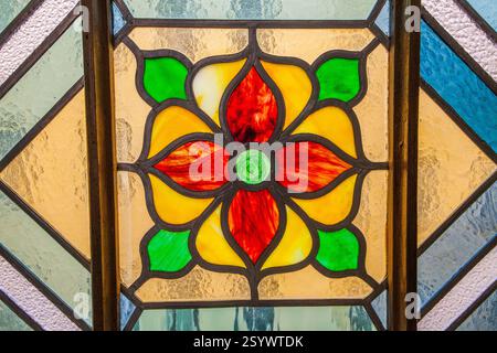 Close-up shot of a stained glass panel showcasing a central floral medallion with vibrant red, yellow, and green hues, surrounded by textured glass in Stock Photo