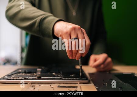 Technician male repairing laptop motherboard, precision screwdriver carefully manipulating electronic components within professional workshop setting. Stock Photo