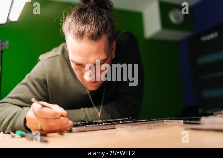 Closeup portrait of skilled technician using tweezers repairing laptop motherboard components in professional electronic workshop setting. Stock Photo