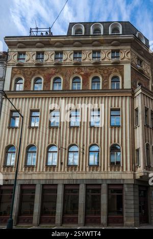 A multi-story building with a decorated facade featuring rows of arched windows, contrasting textures, and a dark-colored upper level under a cloudy s Stock Photo