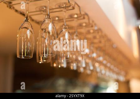 Empty wine glasses hang from a bar rack, likely in a restaurant or bar Stock Photo
