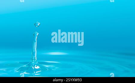 Water drops splashing on calm water surface forming waves against blue background Stock Photo