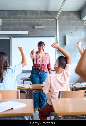 Happy group diverse elementary school students sitting in classroom attending by raising their hands Stock Photo