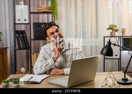 Hispanic businessman freelancer working on laptop and feeling toothache touching mouth with hand, painful expression because of dental illness. Caries, pulpitis, gum disease, dental disease concepts. Stock Photo