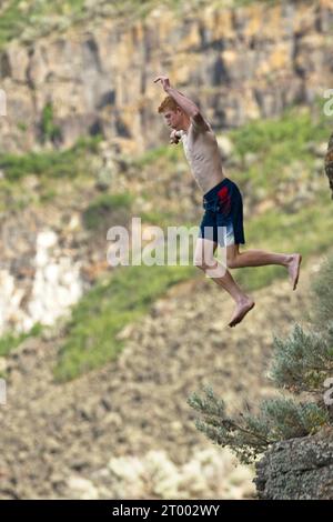 Young man jumps off a rock to the water below. Stock Photo