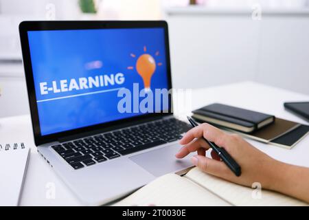 E-learning Education Internet Networking . Young businesswoman sitting at table used laptop with inscription on screen e-learnin Stock Photo