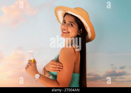 Smiling woman with hat applying sunscreen cream Stock Photo