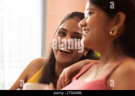 Close-up portrait of two young women sitting together in living room Stock Photo