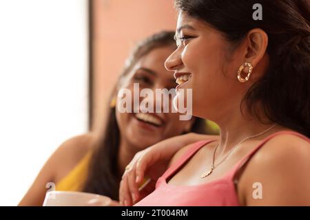 Close-up portrait of two young women sitting together in living room Stock Photo
