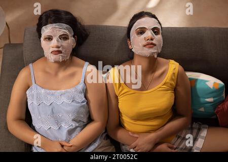 Top angle view of two women with facial mask relaxing on sofa Stock Photo