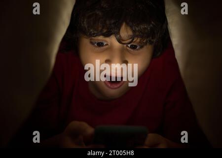 Boy using mobile phone under bed cover at night Stock Photo