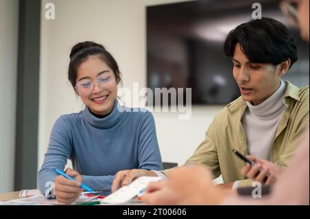 Young smart Asian UI/UX designer working for the project with her team in the meeting room. UX/UI concept. Stock Photo