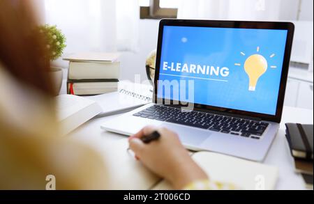 E-learning Education Internet Networking . Young businesswoman sitting at table used laptop with inscription on screen e-learnin Stock Photo