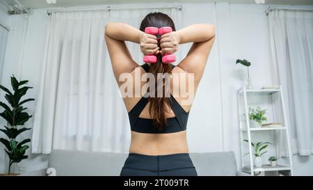 Determined Young Asian healthy woman losing weight training in living room at home and exercising with dumbbells fitness exercis Stock Photo
