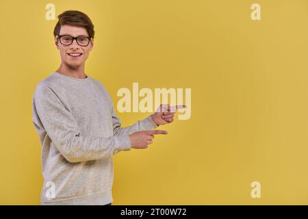 cheerful young man in casual attire pointing two fingers aside on right side on yellow backdrop Stock Photo