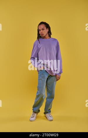 young african american in purple sweatshirt and jeans with dreadlocks posing on yellow background Stock Photo
