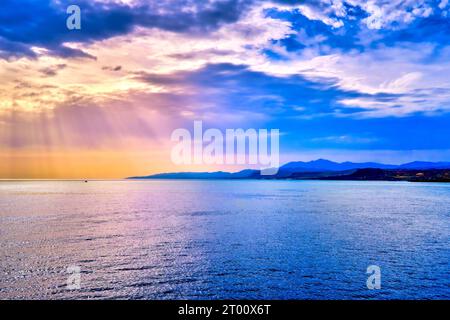 Colorful seascape with colorful clouds and bright sun rays cast over calm sea waters and hazy distant shores. Sunrise or sunset in Mediterranean sea, soft focus background.  Stock Photo