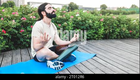 Young man with prostehtic leg doing meditation sitting on yoga mat outdoor - Focus on prosthesis Stock Photo
