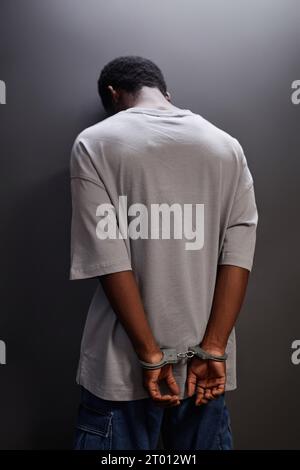 Back view of young Black man arrested standing by wall with handcuffs Stock Photo