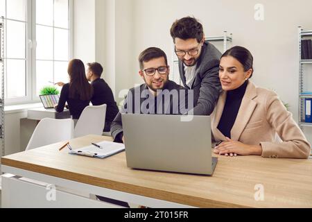 Two interns in office learning new computer software while listening to male business trainer. Stock Photo