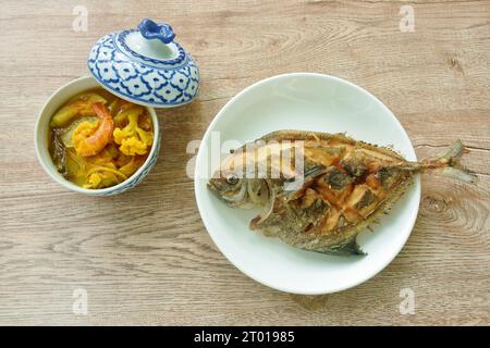 crispy fried black butterfish on plate with boiled spicy mixed vegetable shrimp curry soup in bowl Stock Photo