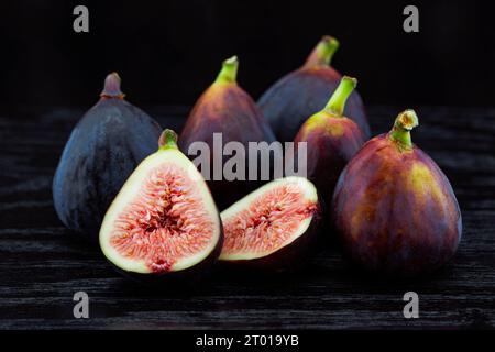 Assortment of cut fig halves and whole figs placed as natural, rustic still life on black wood grain table displays fresh, ripe fruit Stock Photo