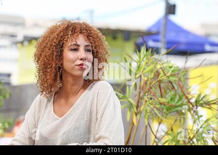 Curly hair woman in white sweater and red pants having a good time outside under a palmer tree in a tropical country Stock Photo