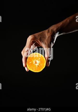Man holding a section of orange and squeezing it, black background, sharp image Stock Photo