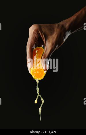 Man holding a section of orange and squeezing it, black background, sharp image Stock Photo