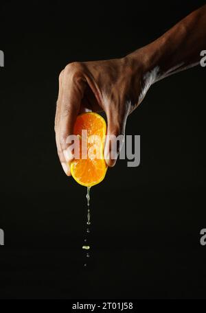 Man holding a section of orange and squeezing it, black background, sharp image Stock Photo