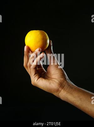 Man holding a section of orange and squeezing it, black background, sharp image Stock Photo
