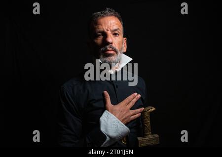 Man dressed in black and white collar with serious gesture that looks like the man from El Greco's Knight of the Hand on the Chest on a black backgrou Stock Photo