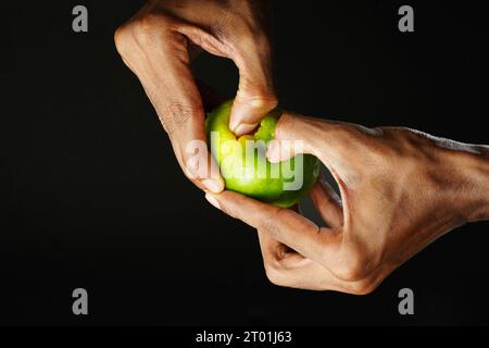 Man holding a section of orange and squeezing it, black background, sharp image Stock Photo