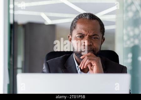 Close-up photo. Senior African American male businessman, director sits in the office at the laptop and looks thoughtfully at the screen. Stock Photo