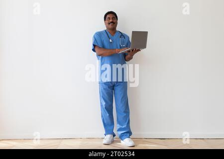 Online Consultation Service. Portrait Of Smiling Confident Indian Doctor Using Laptop Stock Photo