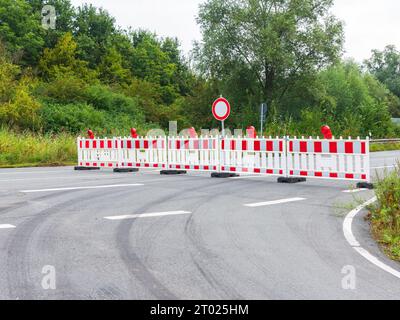 Asphalt road is blocked with a red and white plastic barriers due to construction work. Roadwork, no passage prohibited Stock Photo