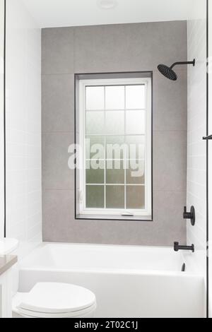 A luxury shower with white subway and brown tile walls, black faucet, and a white framed window with frosted glass. Stock Photo