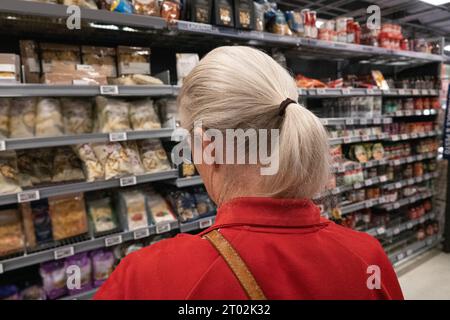 Woman shopping in food department of a supermarket. Close up of woman seen from behind  with blond hair and red sweatshirt. Stock Photo