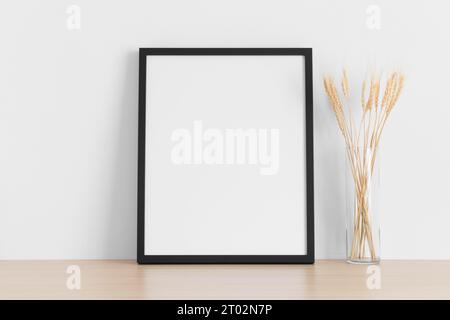 Black frame mockup with dried flowers on the wooden table. Stock Photo