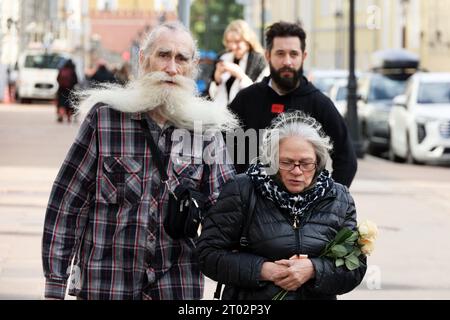 Elderly couple walking on city street holding hands. Man with long white beard and woman with bouquet of flowers Stock Photo