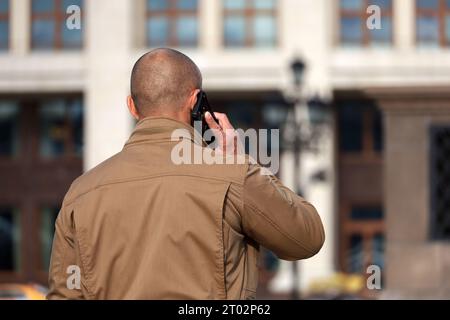 Man with shaved head talking on mobile phone on a city street. Concept of cellular communication Stock Photo