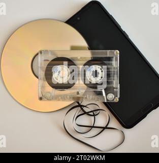 New and old ways of transporting music, a compact disc, an audio cassette tape with some of the tape unravelled and a mobile phone. Stock Photo