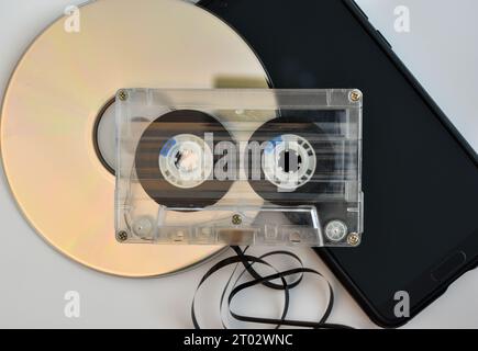 New and old ways of transporting music, a compact disc, an audio cassette tape with some of the tape unravelled and a mobile phone. Stock Photo